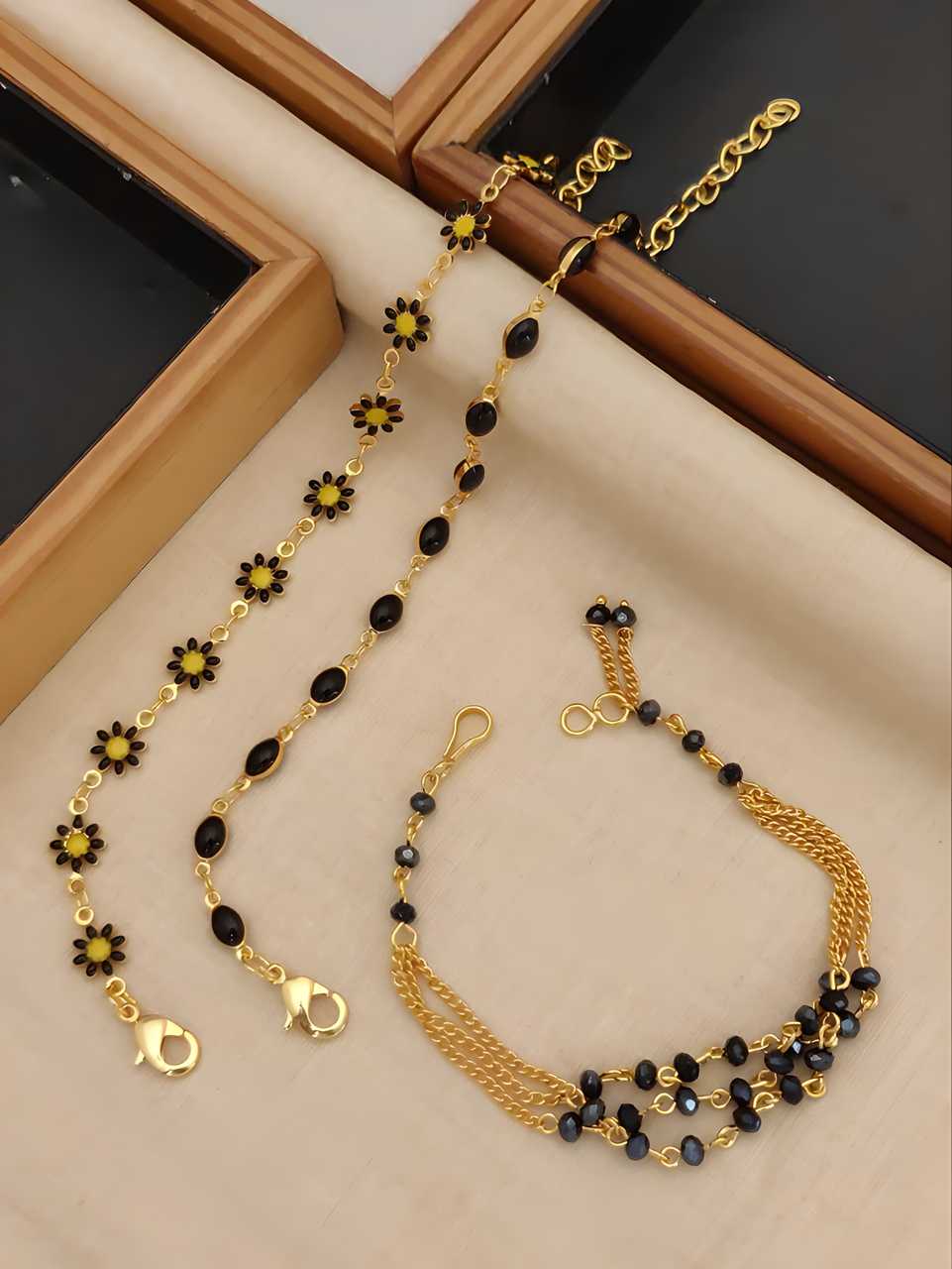 Gold bracelets with black and yellow beads on a beige surface