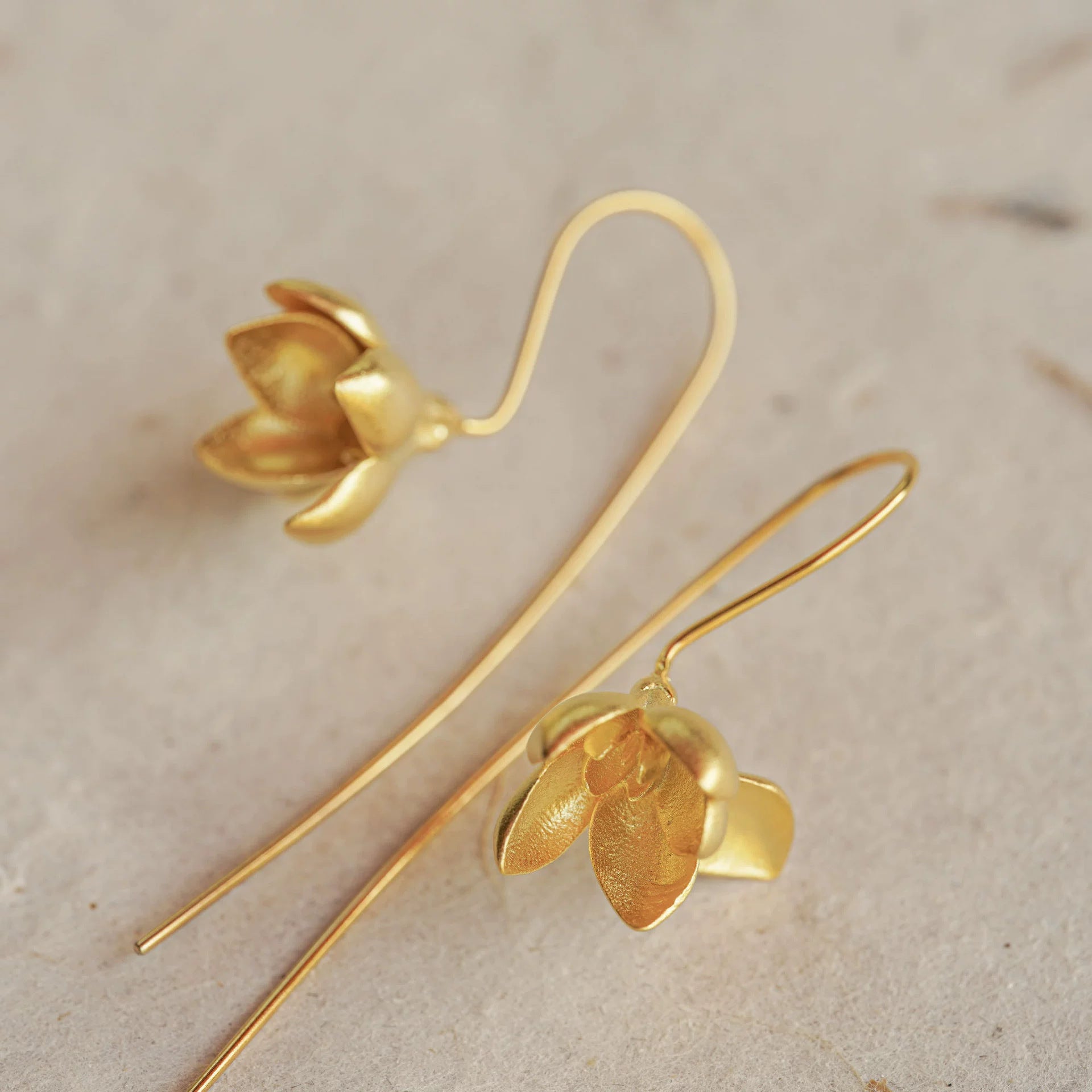 Gold flower-shaped earrings on a beige background
